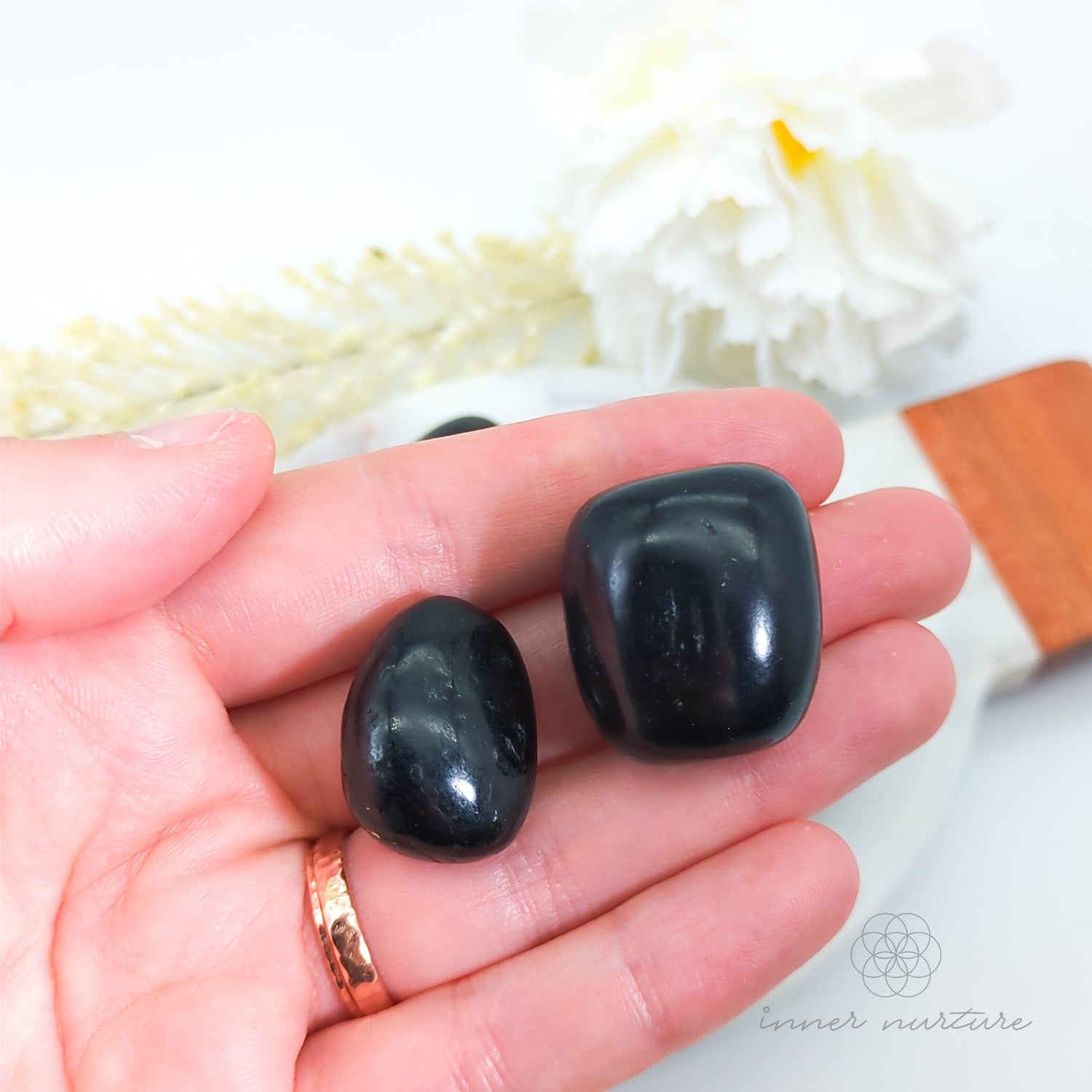 Two black stones held in a hand with a blurred natural background. Black Tourmaline tumbles available at Inner Nurture, an online crystal shop in Australia.