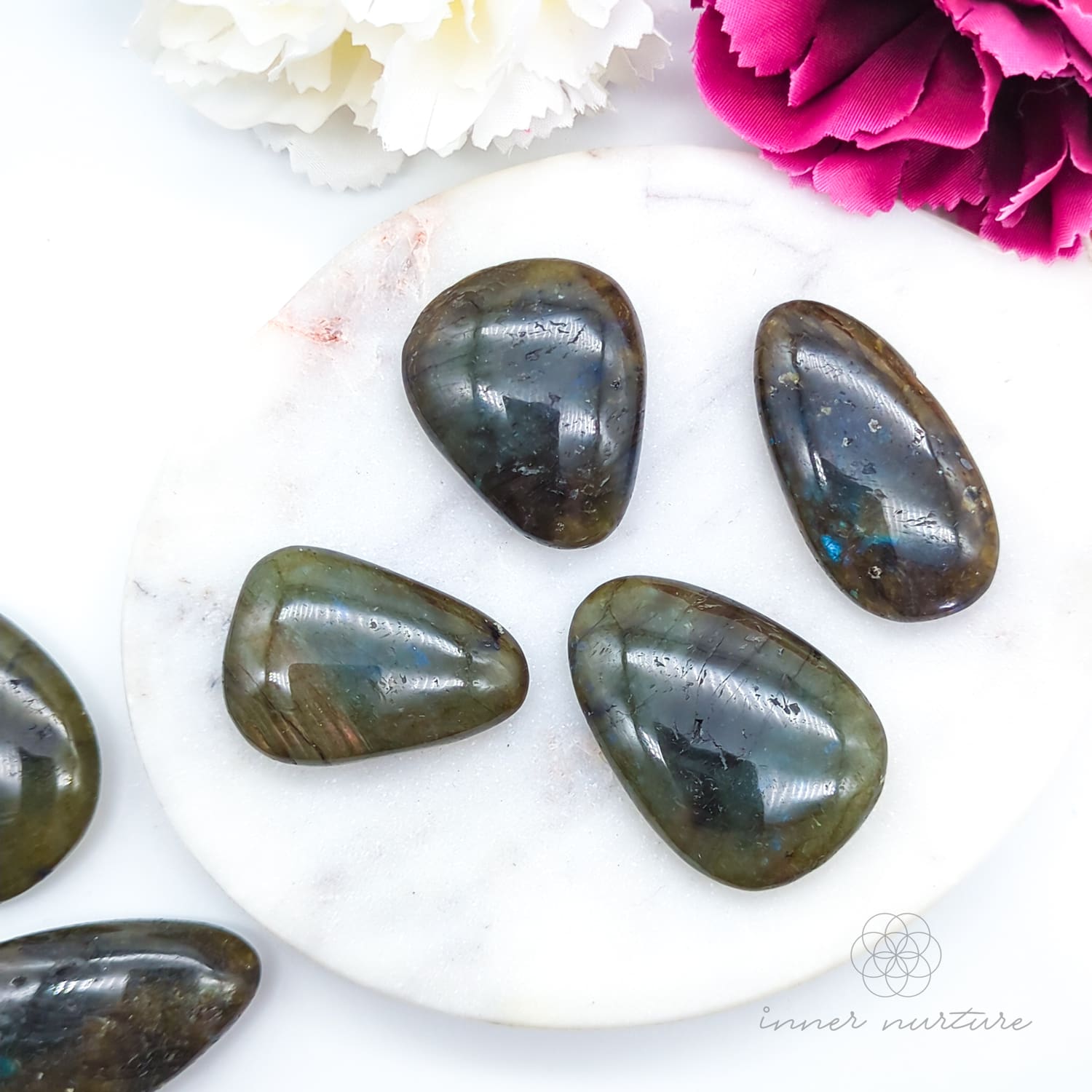 Polished labradorite stones on a white surface with flowers.  Labradorite palm stone available at Inner Nurture, an online crystal shop in Australia.
