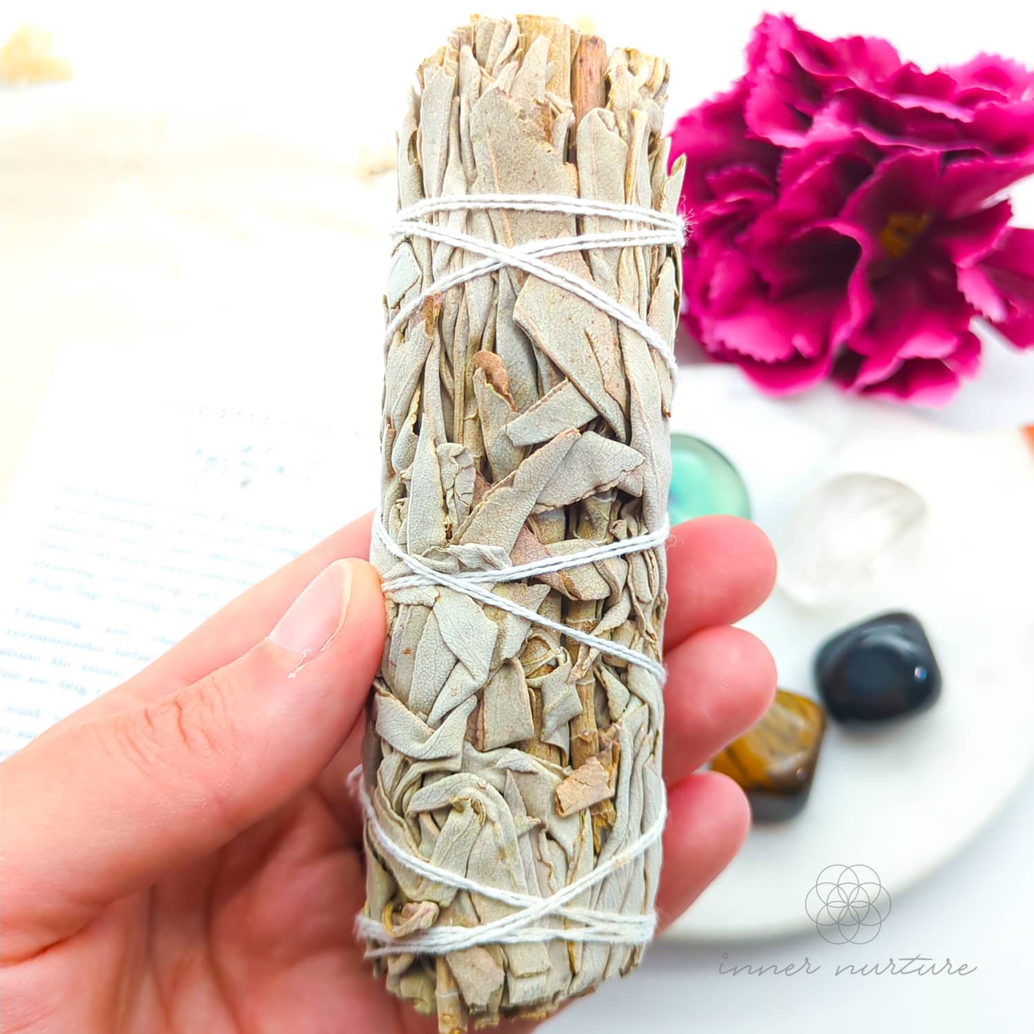 Hand holding a smudge stick with flowers and stones in the background. Essentials Crystal Kit, available on line in Australia at Inner Nurture