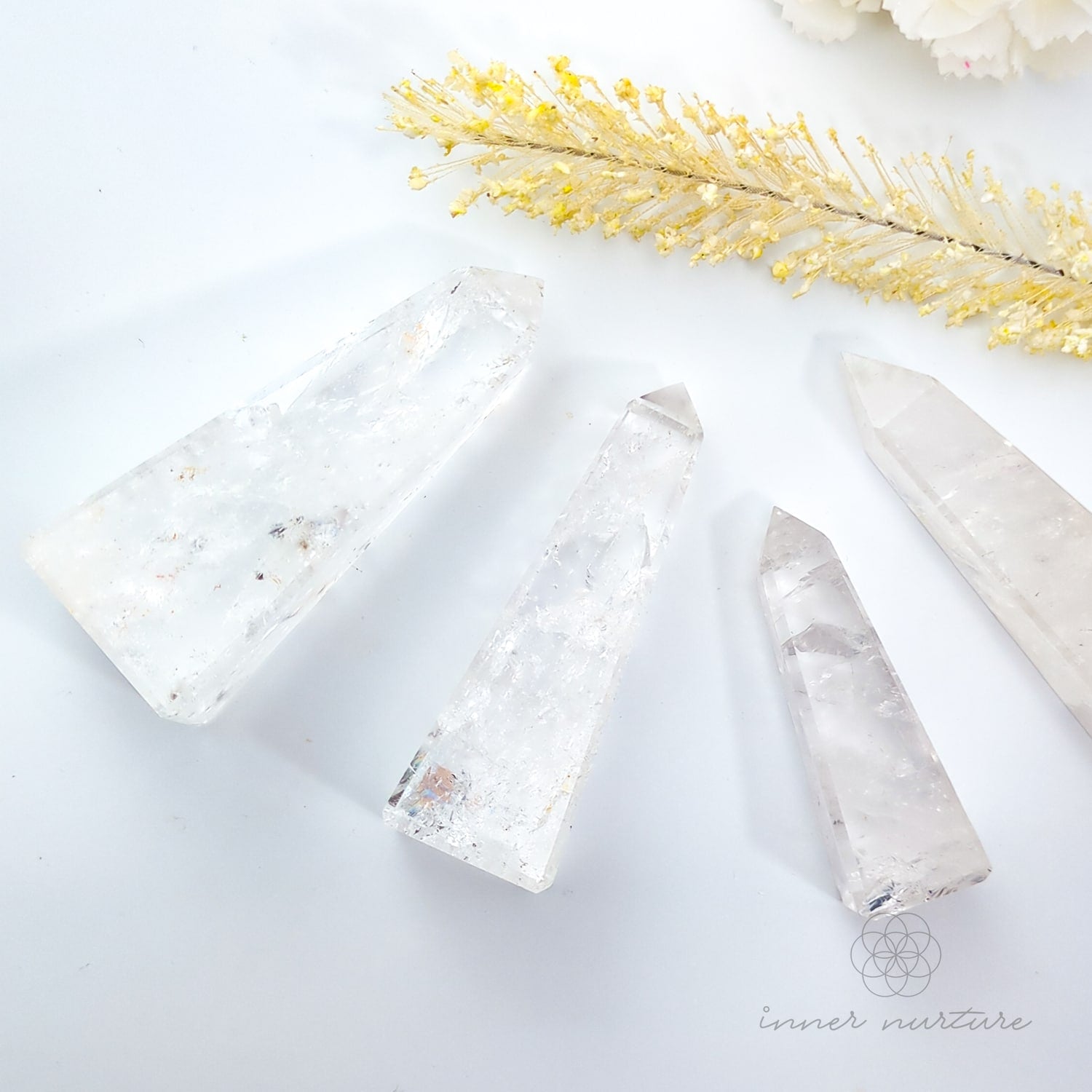 Crystal objects on a white surface with decorative yellow flowers. Clear Quartz Tower for Clarity & Energy | Crystals Australia Inner Nurture