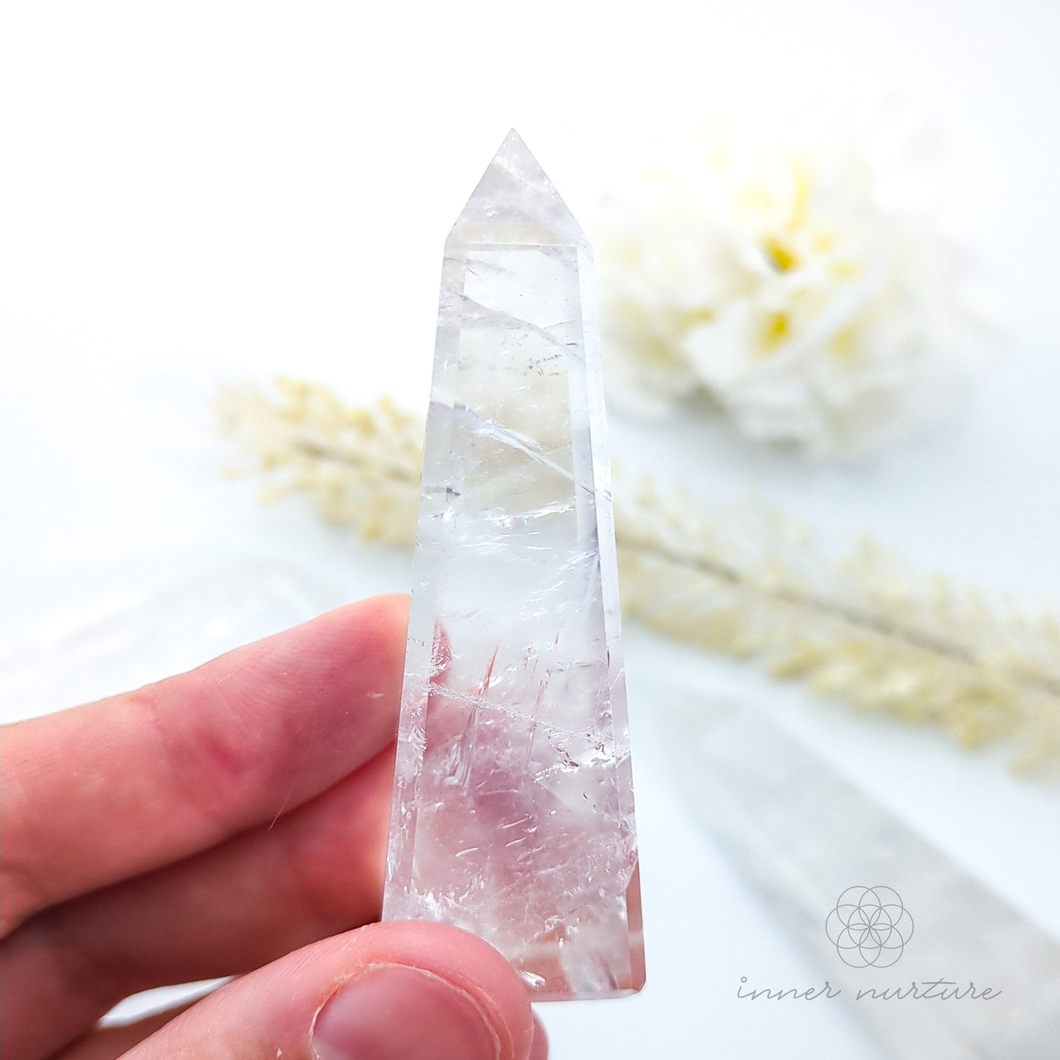 Clear crystal held by a hand with a blurred natural background. Clear Quartz Tower for Clarity & Energy | Crystals Australia Inner Nurture