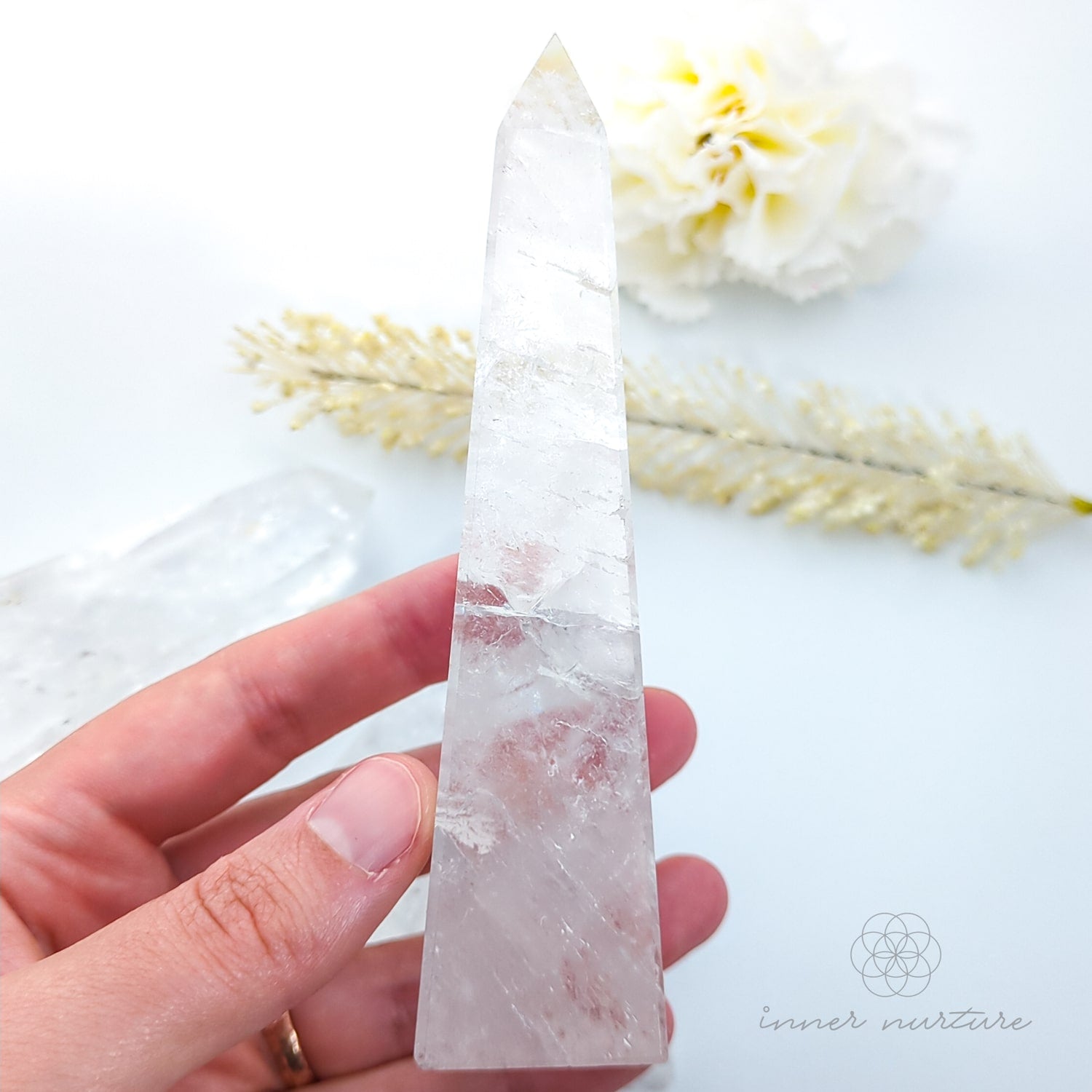 Clear crystal held by a hand with a blurred natural background. Clear Quartz Tower for Clarity & Energy | Crystals Australia Inner Nurture