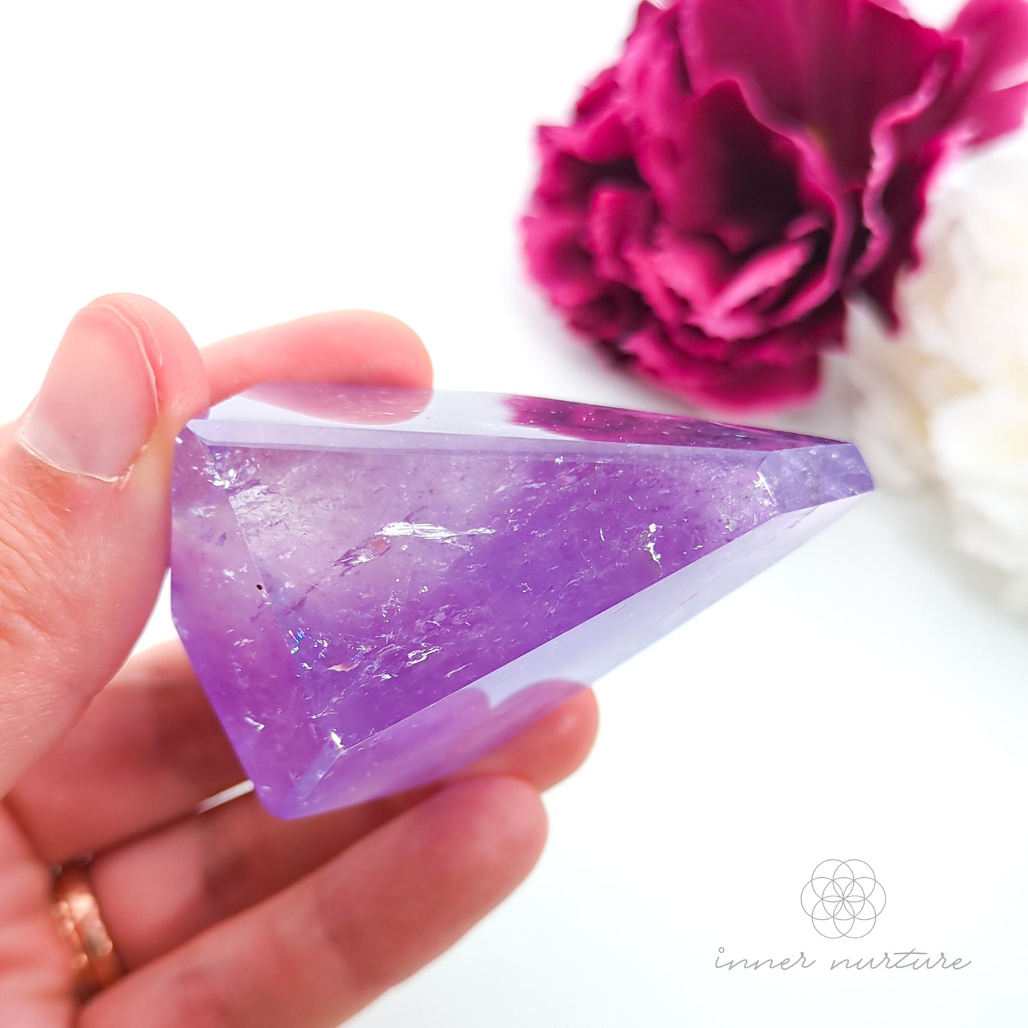 Hand holding a purple crystal with pink flowers in the background. Amethyst Free Form #3 for Calm & Clarity | Crystals Australia