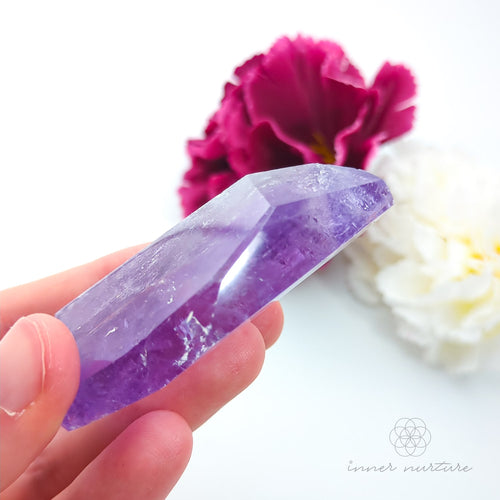 Hand holding a purple crystal with flowers in the background. Amethyst Free Form #3 for Calm & Clarity | Crystals Australia