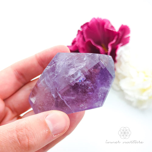 Hand holding a purple crystal with flowers in the background. Amethyst Free Form #2 for Calm & Clarity | Crystals Australia