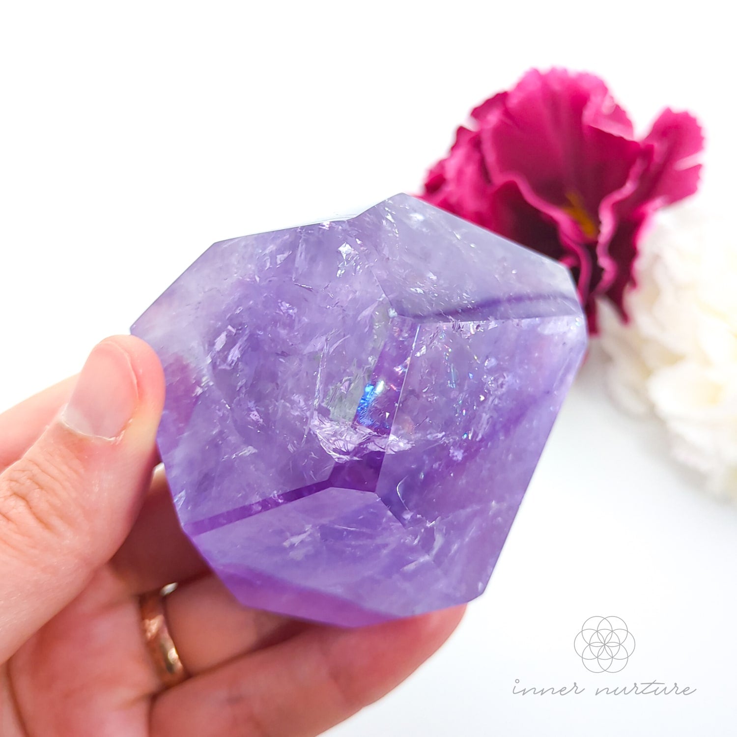 Hand holding a purple crystal with pink flowers in the background. Amethyst Free Form #1 for Calm & Clarity | Crystals Australia