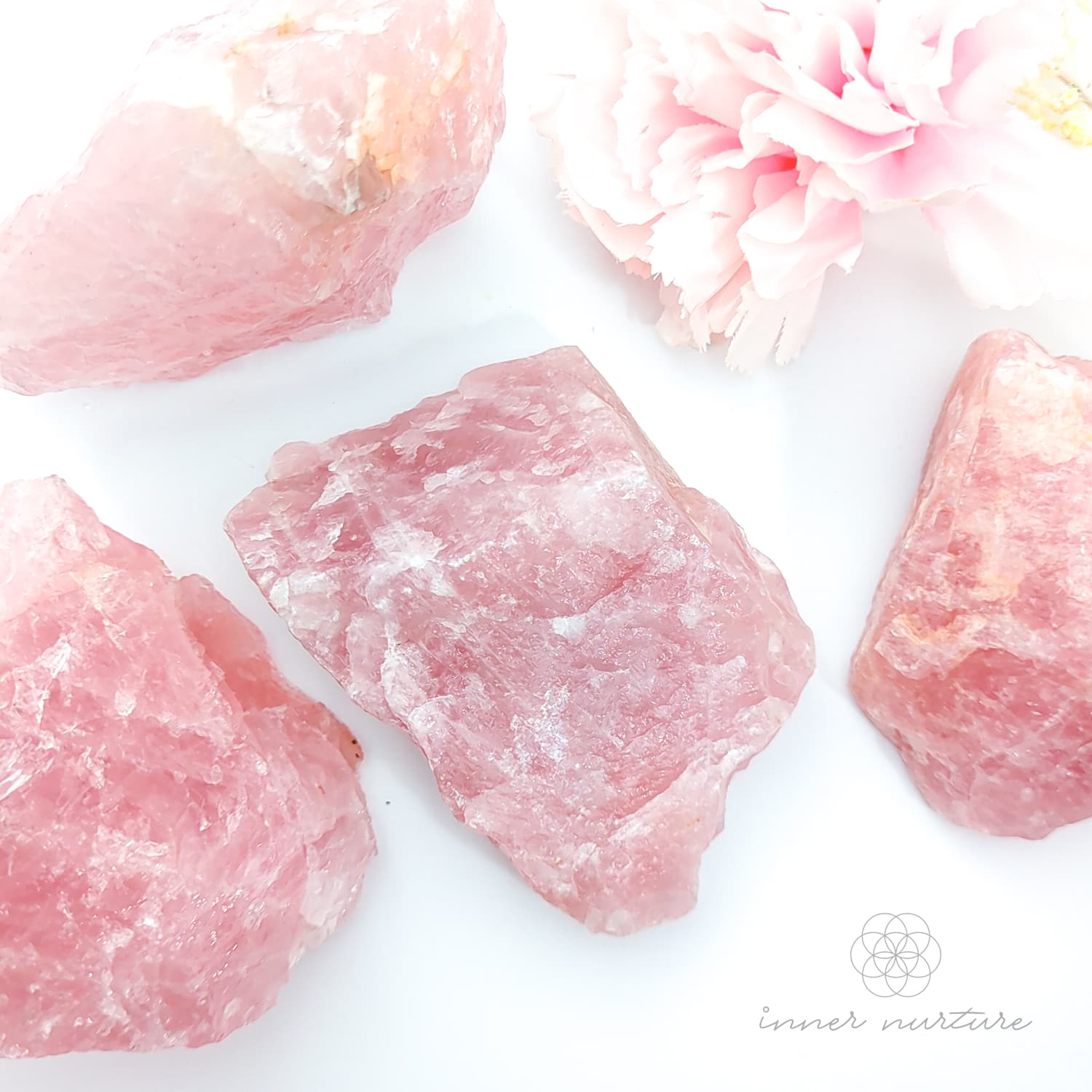Pink crystals on a white background with a floral element. Rose Quartz raw crystal available online at Inner Nurture Crystals Australia