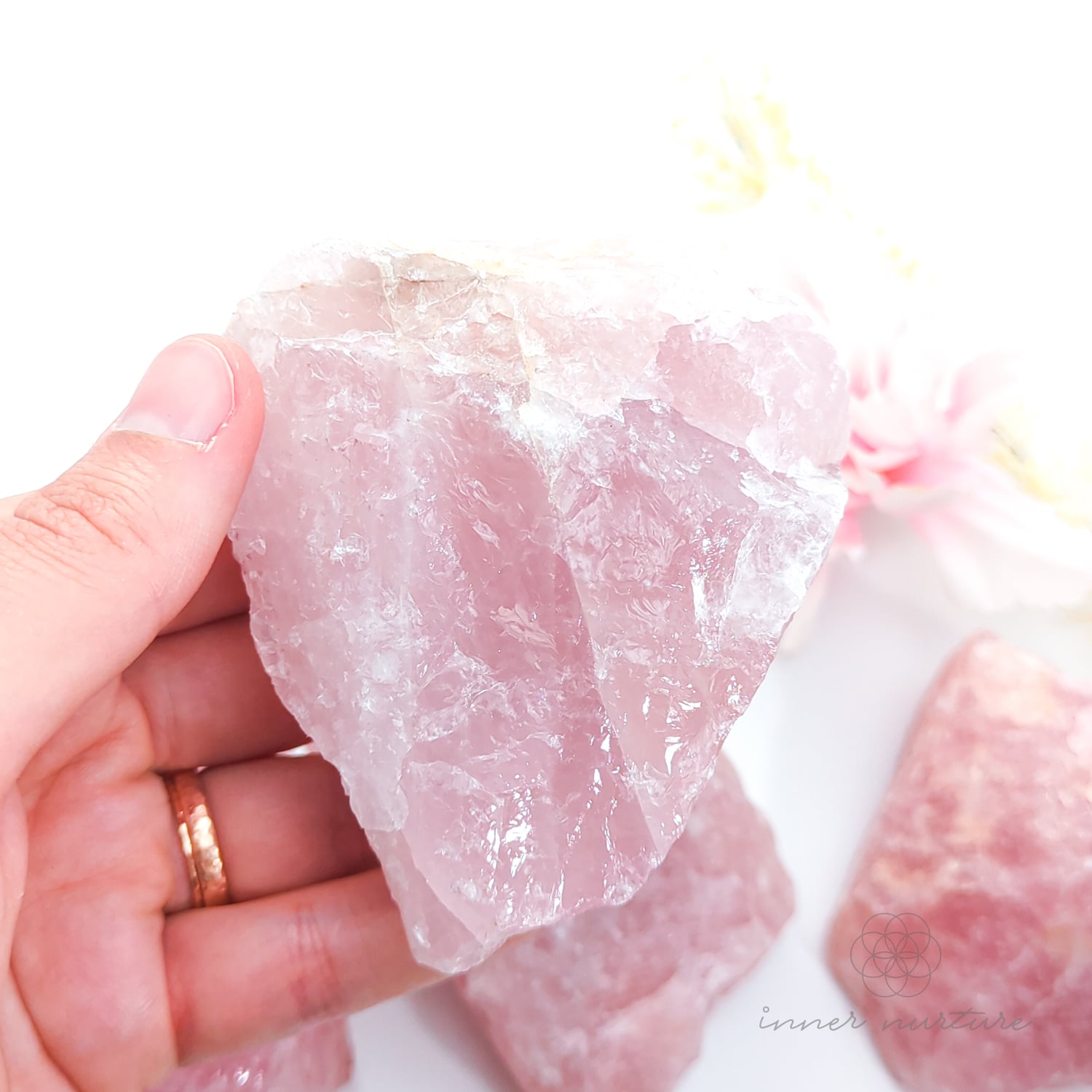 Hand holding a rough pink stone crystal against a white background. Rose Quartz raw crystal available online at Inner Nurture Crystals Australia