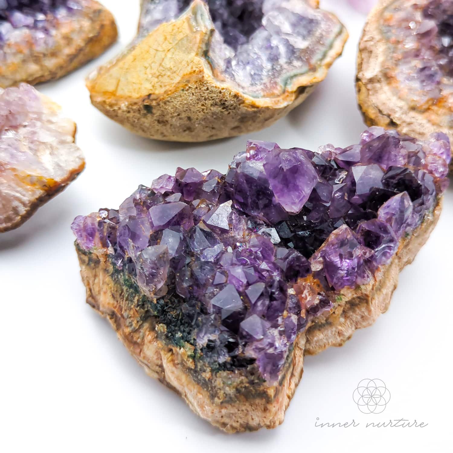 Close-up of amethyst crystal clusters on a white background with 'inner nurture' branding. Amethyst crystal cluster available online at Inner Nurture Crystals Australia