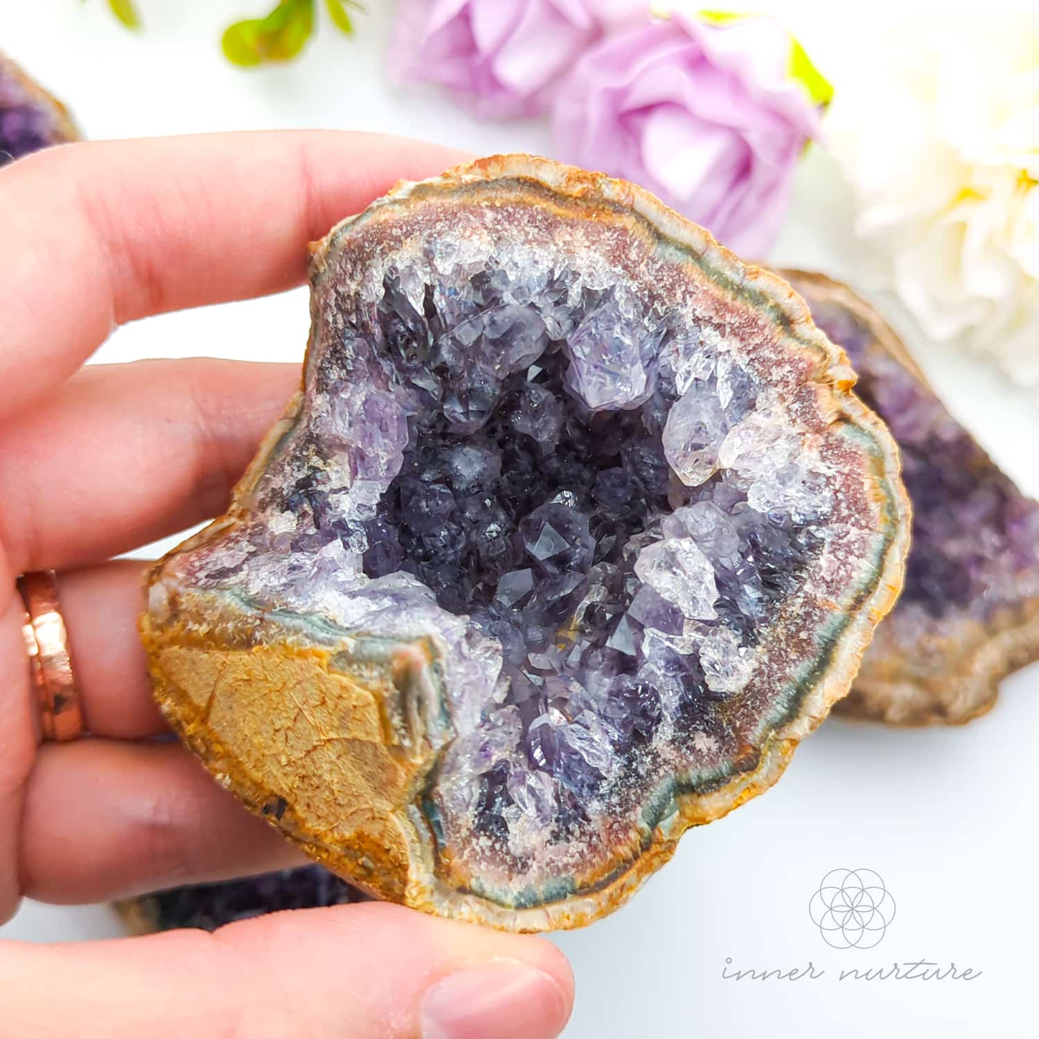 Hand holding a geode crystal with a blurred floral background. Amethyst crystal cluster available online at Inner Nurture Crystals Australia