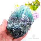 Hand holding a large crystal with a colorful blurred background. Rainbow Fluorite Specimen #1 for Balance & Clarity | Crystals Australia