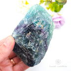 Hand holding a large crystal with a colorful blurred background. Rainbow Fluorite Specimen #1 for Balance & Clarity | Crystals Australia