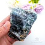 Hand holding a large blue crystal with a blurred floral background. Rainbow fluorite available at Inner Nurture crystals australia