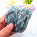 Hand holding a large blue crystal with a blurred floral background. Rainbow fluorite available at Inner Nurture crystals australia