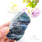 Raw fluorite crystal held by a hand with a soft focus floral background .Rainbow Fluorite available at Inner Nurture crystals in Australia