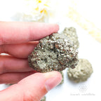 Hand holding a metallic rock with a blurred natural background. Pyrite crystal cluster available online at Inner Nurture Crystals Australia