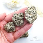 Three pyrite crystals held in a hand with a blurred natural background. Pyrite crystal cluster available online at Inner Nurture Crystals Australia