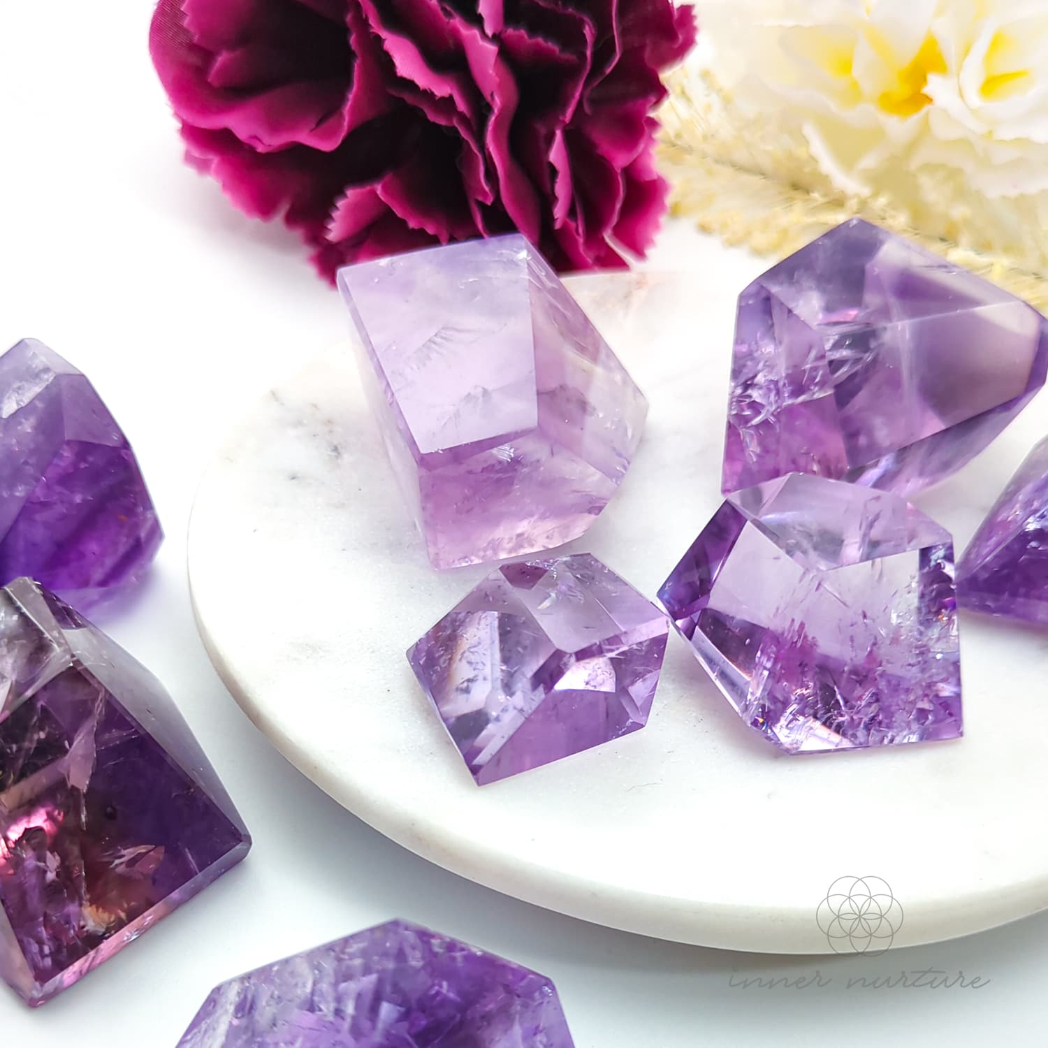 Purple crystal-like objects on a white plate with flowers in the background. Amethyst Free Form for Calm & Clarity | Crystals Australia