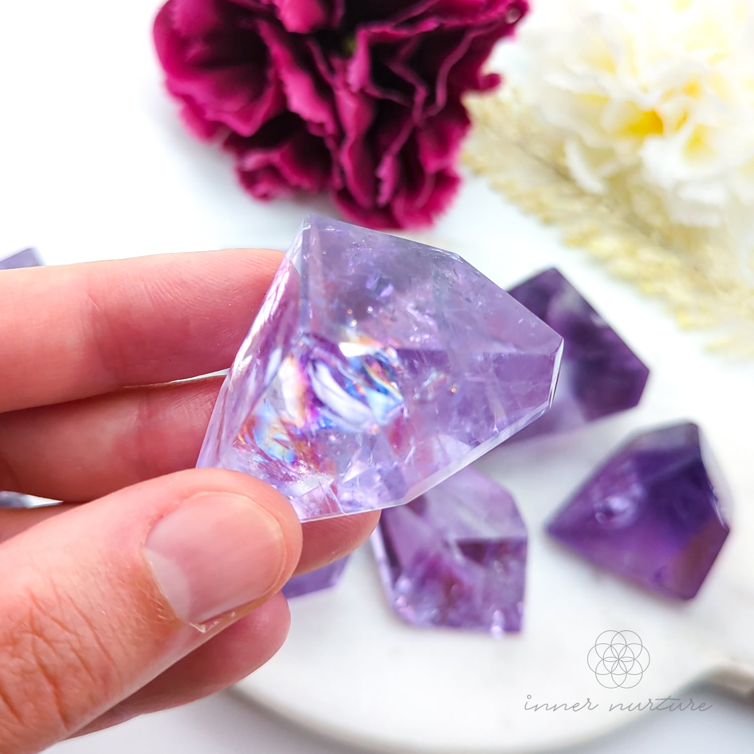 Hand holding a purple crystal with flowers in the background. Amethyst Free Form for Calm & Clarity | Crystals Australia