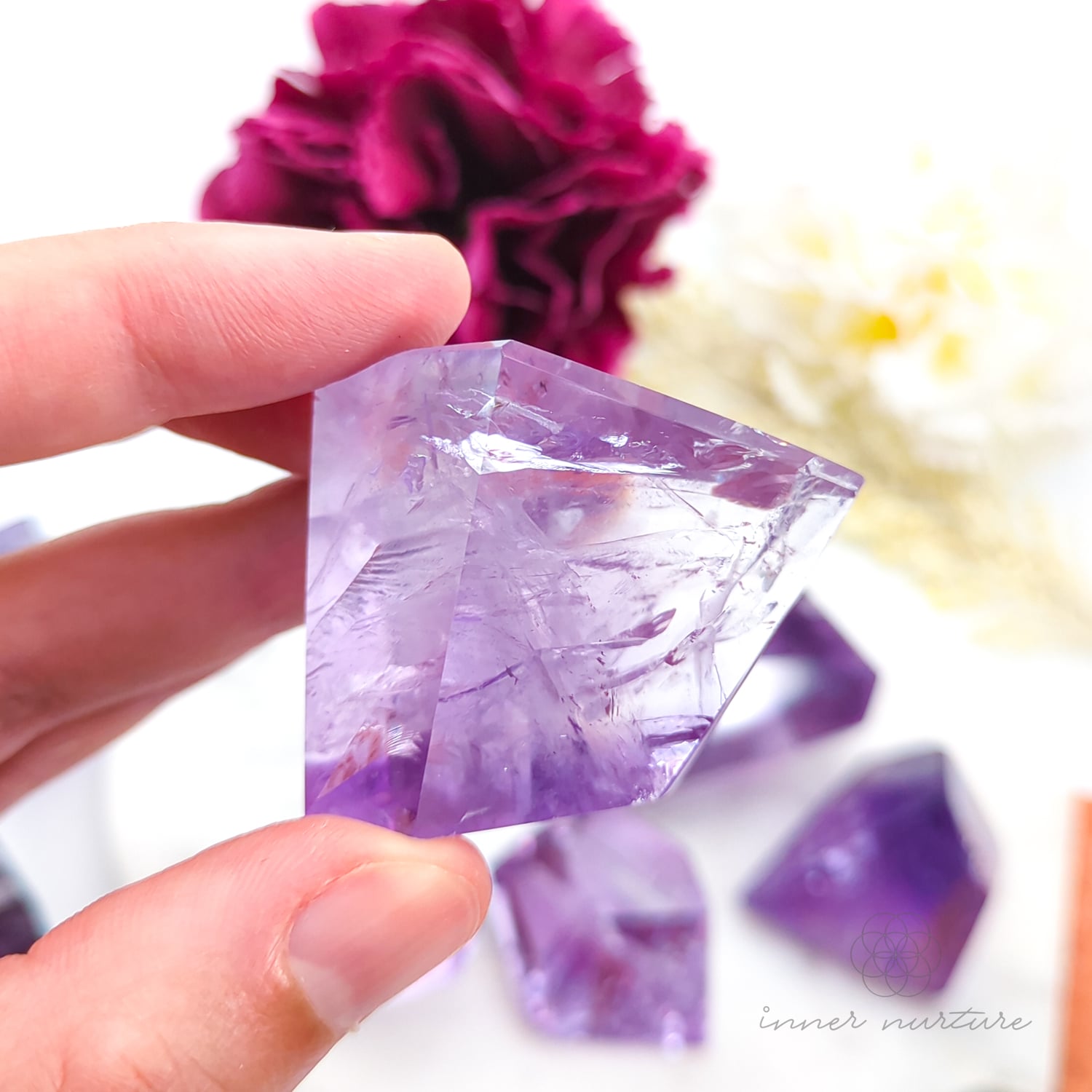 Hand holding a purple crystal with flowers in the background. Amethyst Free Form for Calm & Clarity | Crystals Australia