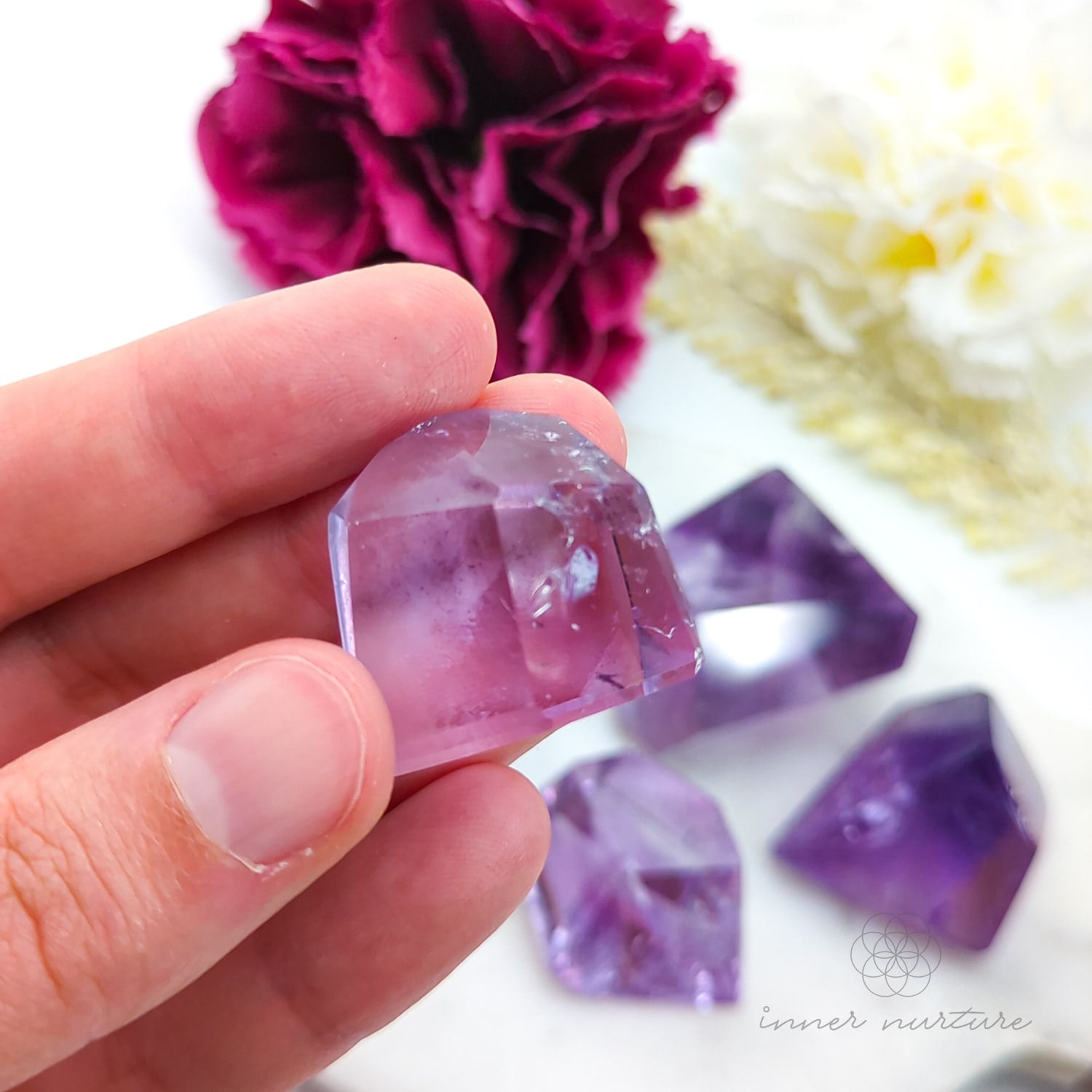 Hand holding a purple crystal with flowers in the background. Amethyst Free Form for Calm & Clarity | Crystals Australia