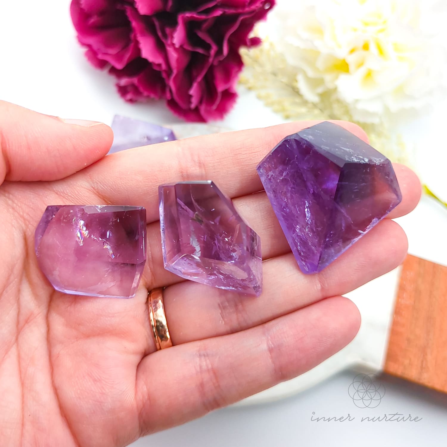 Hand holding a purple crystal with flowers in the background. Amethyst Free Form for Calm & Clarity | Crystals Australia