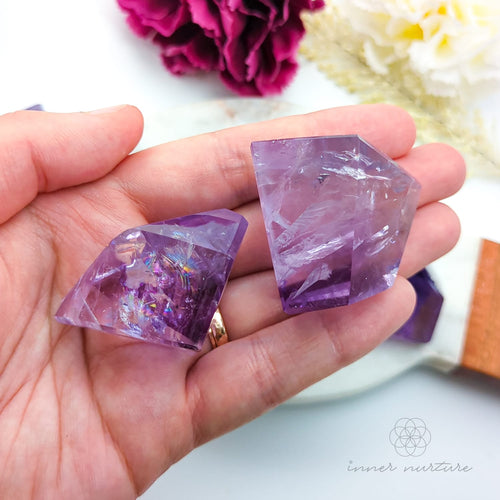 Hand holding a purple crystal with flowers in the background. Amethyst Free Form for Calm & Clarity | Crystals Australia