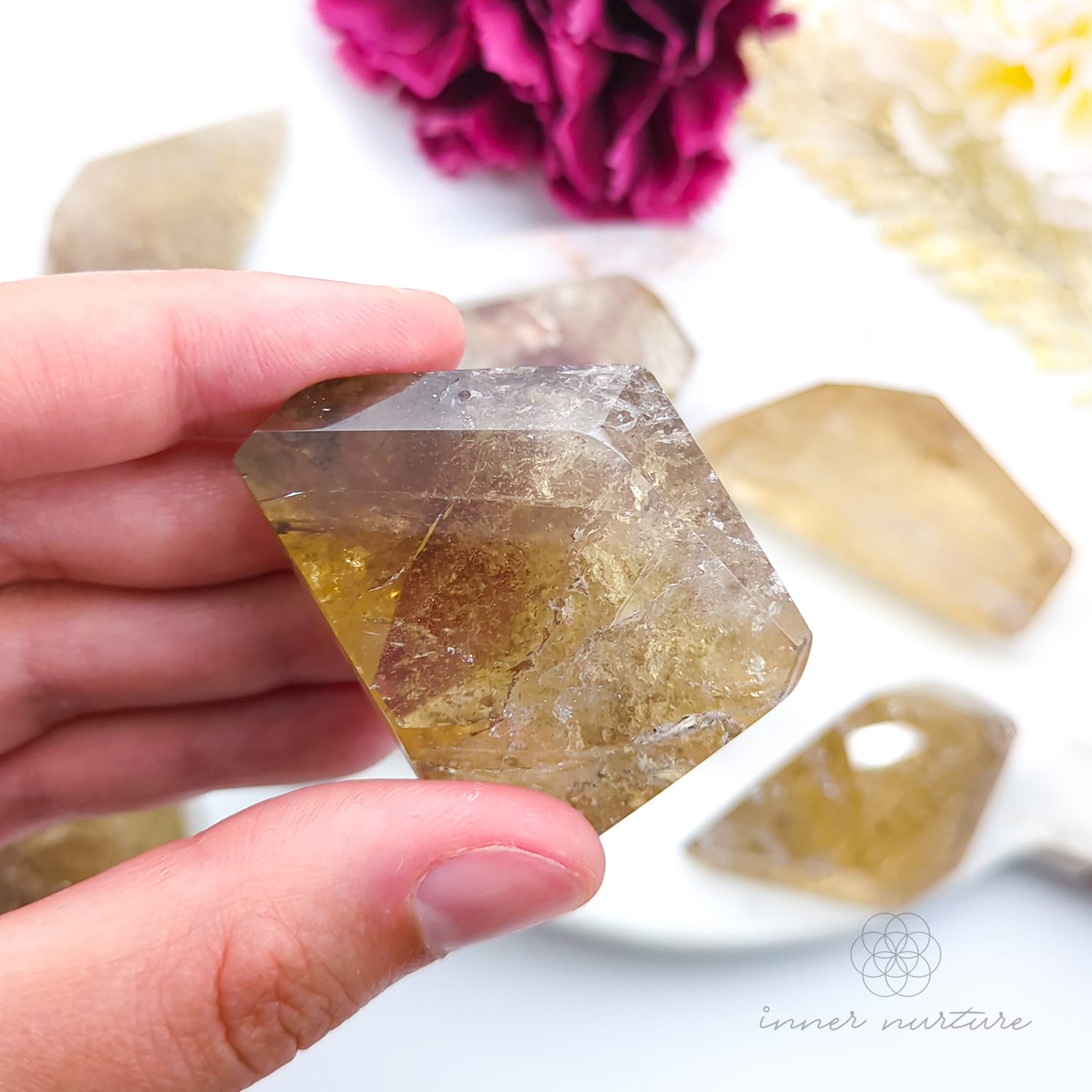 Hand holding a hexagonal crystal with blurred crystals and flowers in the background. Citrine (Natural) Free Form for Abundance & Manifestation | Crystals Australia Inner Nurture