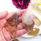 Hand holding two crystal points with a blurred background of flowers. Citrine (Natural) Free Form for Abundance & Manifestation | Crystals Australia Inner Nurture