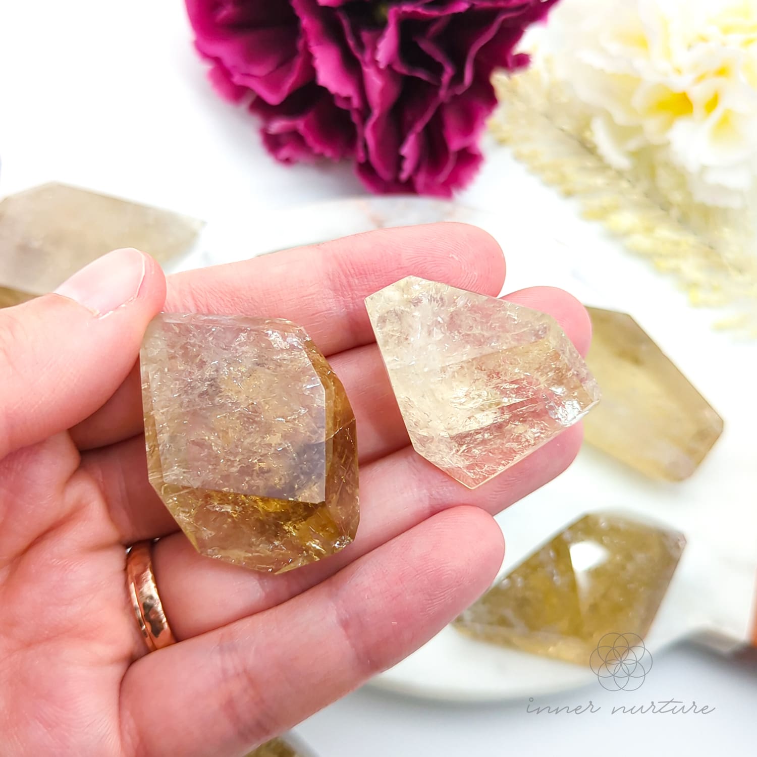 Hand holding two clear crystal stones with a blurred background of flowers. Citrine (Natural) Free Form for Abundance & Manifestation | Crystals Australia Inner Nurture