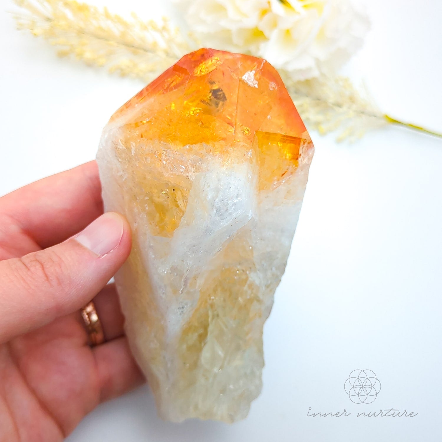 Hand holding a crystal with orange and white colors on a light background. Citrine crystal point available online at Inner Nurture Crystals Australia