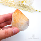 Hand holding a crystal with a white background and decorative elements. Citrine crystal available online at Inner Nurture Crystals Australia