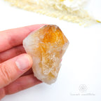Hand holding a clear crystal with yellow-orange center on a white background. Citrine crystal available online at Inner Nurture Crystals Australia