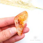 Hand holding a rough orange crystal against a white background. Citrine crystal available online at Inner Nurture Crystals Australia