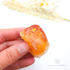 Hand holding a orange crystal with a blurred natural background. Citrine crystal available online at Inner Nurture Crystals Australia