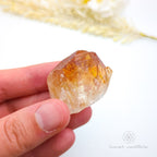Hand holding a clear crystal with yellowish tint against a white background. Citrine crystal available online at Inner Nurture Crystals Australia