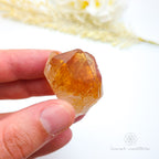 Hand holding a clear crystal with a blurred natural background. Citrine crystal available online at Inner Nurture Crystals Australia