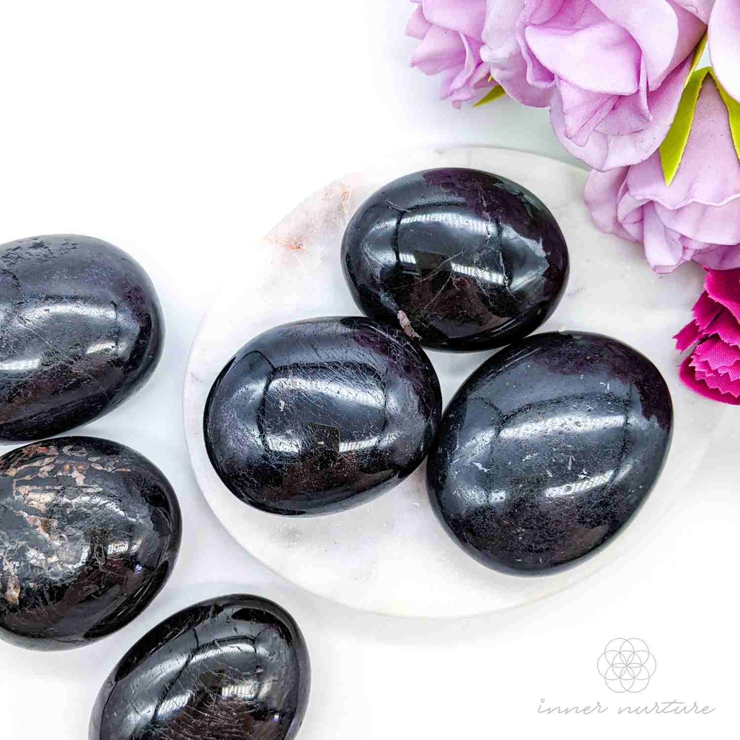 Black stones on a white plate with pink flowers -  Black Tourmaline palm stones sold online by Inner Nurture, with Australia wide shipping. 
