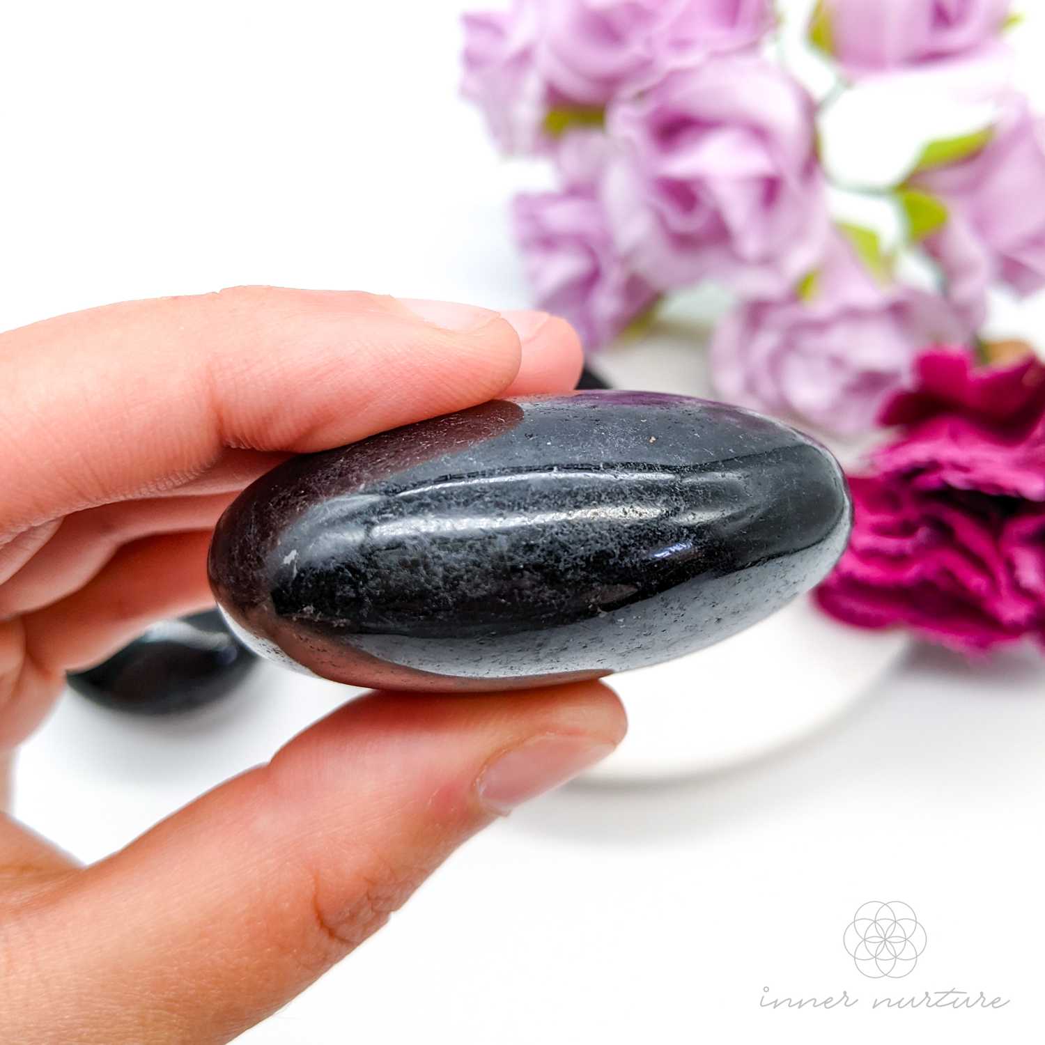 Black stones on a white plate with pink flowers -  Black Tourmaline palm stones sold online by Inner Nurture, with Australia wide shipping. 