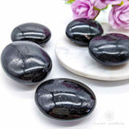 Black stones on a white plate with pink flowers -  Black Tourmaline palm stones sold online by Inner Nurture, with Australia wide shipping. 