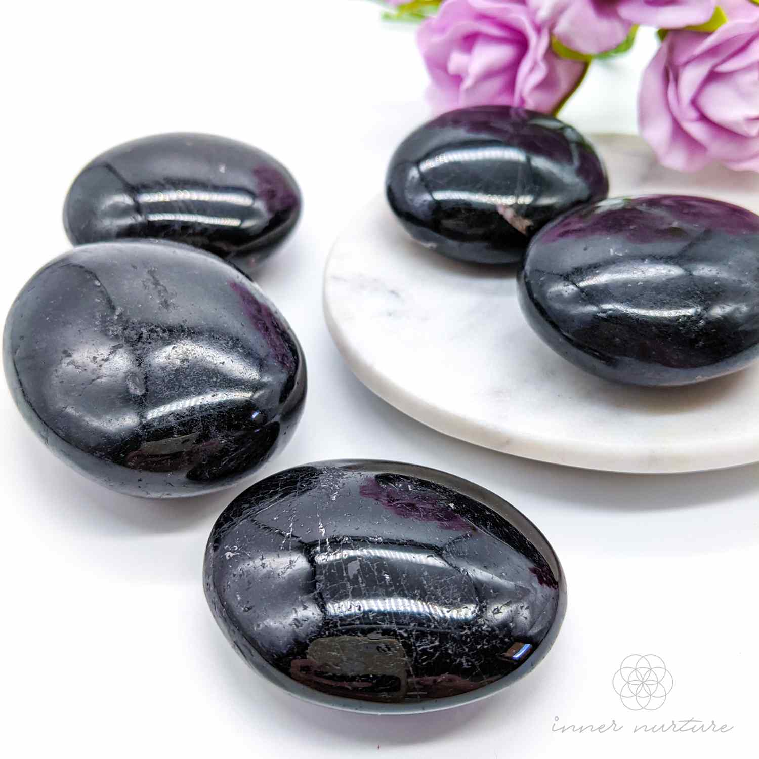 Black stones on a white plate with pink flowers -  Black Tourmaline palm stones sold online by Inner Nurture, with Australia wide shipping. 