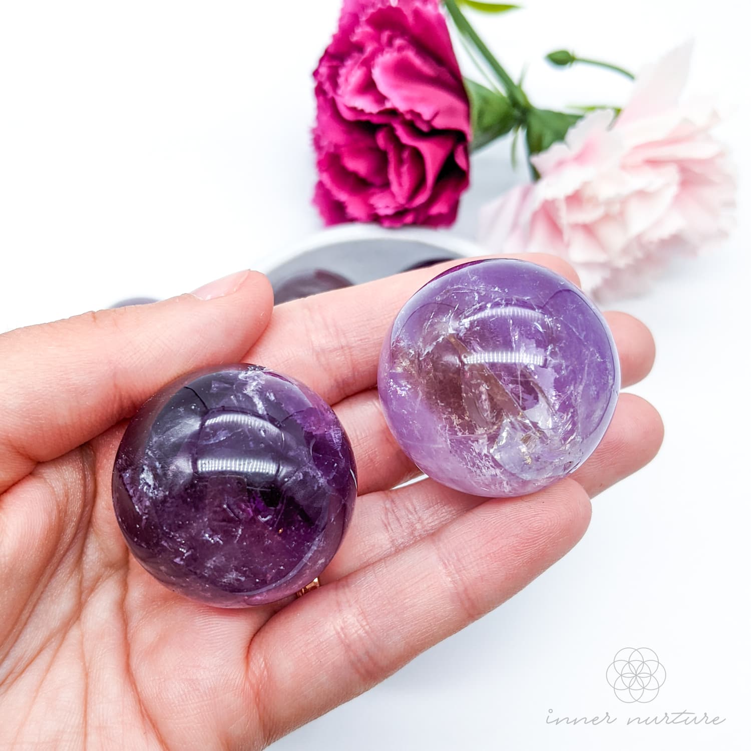 Hand holding a purple crystal ball with flowers in the background. Amethyst sphere available at Inner Nurture, an online crystal shop in Australia. 